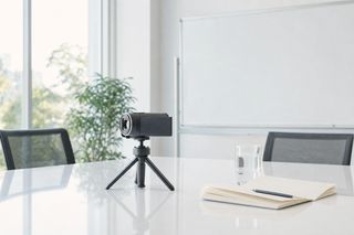 明るい会議室のテーブルに置かれた三脚付きの小型ビデオカメラ