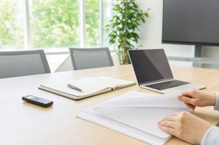 明るい会議室のテーブルに置かれたICレコーダーとノートパソコン、重ねられた見積書の紙
